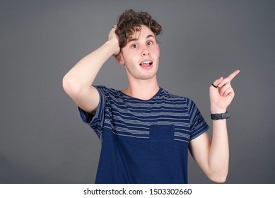 Portrait of young man with shocked facial expression, showing something amazing on blank space, one hand on her head and pointing with forefinger. 