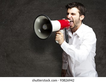 Portrait Of A Young Man Shouting With A Megaphone Against A Black Background