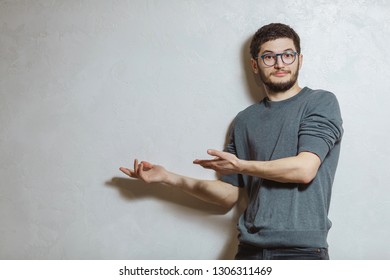 Portrait of young man showing with hands on wall, over white textured background.