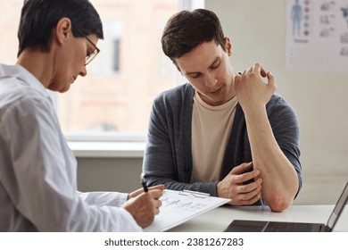 Portrait of young man showing skin rash to doctor during consultation in dermatology clinic - Powered by Shutterstock