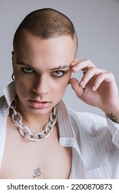 Portrait Of Young Man With Smoky Eyes Makeup And Partly Shaved Brows Posing Over Grey Studio Background. Green Eyes. Concept Of Fashion, Freedom Of Choice, Lifestyle, Lgbt, Generation Z, Trends