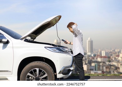 Portrait of a young man standing in front of a broken car on the road Looking at the car engine and talking on the phone