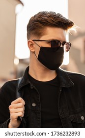 Portrait Young Man In Sunglasses In Stylish Clothes In Black Protective Mask In Bright Spring Day. Stylish Hipster Guy Is Walks In Mask On The City. Covid-19 Virus Protection Concept.No To Coronavirus