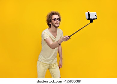 Portrait of young man in sunglasses taking selfie using monopad.Studio shot.Yellow background.Isolate.
