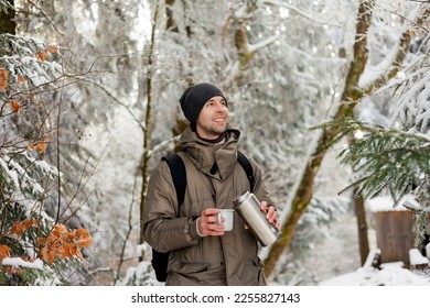 Portrait of young man in warm clothes in winter forest. Drinking hot tea outdoors from thermos. Hiking. - Powered by Shutterstock