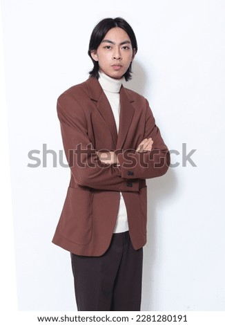 portrait of young man wearing brown suit, sweater with arms crossed posing on white background,