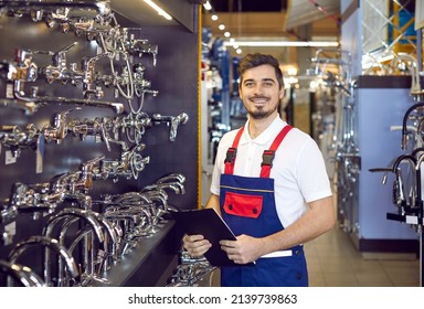 Portrait of a young man who sells faucets. Happy salesman in uniform standing in the aisle with modern water taps at a big hardware store or shopping mall