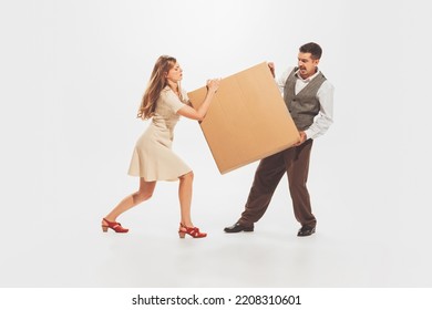 Portrait Of Young Man And Woman Carrying Heavy Cardboard Box Isolated Over White Studio Background. Moving Into New Apartment. Shopping. Concept Of Retro Fashion, Style, Youth Culture, Emotions, Ad