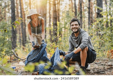 Portrait of young man and woman picking up trash from forest with look in camera. Young couple volunteers eco-savers protecting wood from pollution with plastic - Powered by Shutterstock