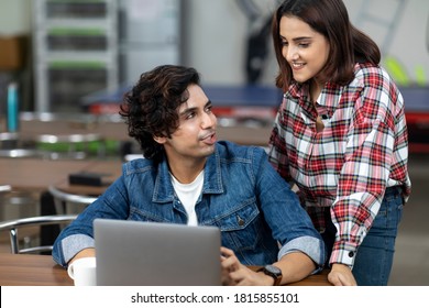 Portrait Of A Young Man And Woman Working On Their Laptop In An Office Cafeteria, Coffee Shop, Casual Work Environment.