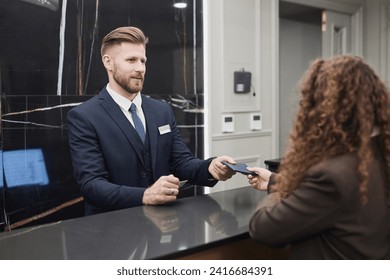 Portrait of young man working at hotel reception desk and taking documents of guest for check in - Powered by Shutterstock