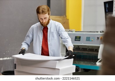 Portrait Of Young Man Working In Print Shop And Holding Stack Of Paper, Copy Space