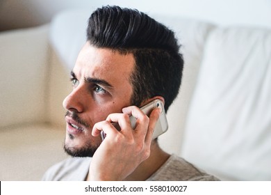 Portrait Of A Young Man Worried Taking A Phone Call On His Smart Phone In His Home - Angry Man In A Bad Mood Having Some Discussion Using Cellphone