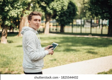 Portrait Of Young Manager Or Ceo Holding White Tablet Pc With Black Touchscreen. Male Wear Casual Clothes And Standing On The Street In Sunny Day With Portable Gadget. Image With Copy Space.
