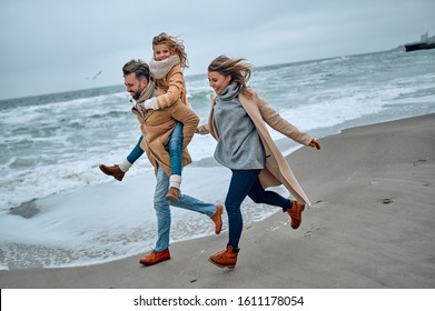 Portrait of a young married couple and their cute daughter who have fun on the beach in winter. - Powered by Shutterstock