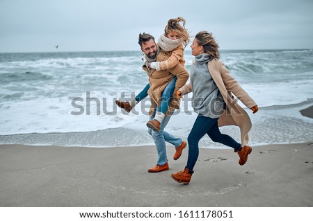 Portrait of a young married couple and their cute daughter who have fun on the beach in winter.