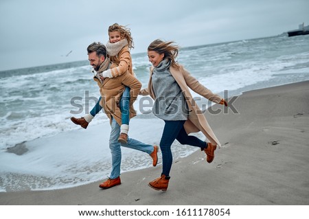 Portrait of a young married couple and their cute daughter who have fun on the beach in winter.