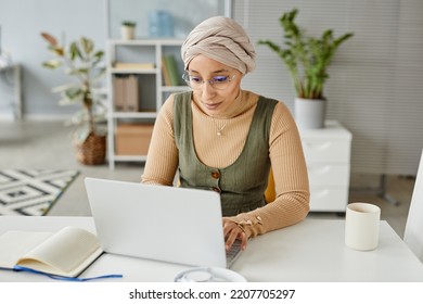 Portrait of young Middle Eastern businesswoman wearing headwrap in office and typing at laptop - Powered by Shutterstock