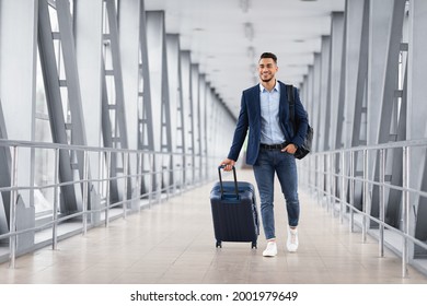 Portrait of young middle eastern man walking in airport terminal with luggage, smiling arab guy carrying suitcase while going to boarding gate, enjoying air travels and business trips, copy space - Powered by Shutterstock