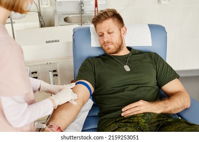 Portrait Of Young Military Man Giving Blood At Donor Center With Nurse Helping, Copy Space