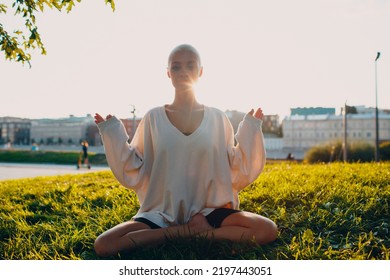 Portrait Of Young Millenial European Short Haired Woman Doing Yoga Lotus Asana On Green Grass Meadow Summer Park Sunset. Beautiful Happy Blonde Girl Outdoor.