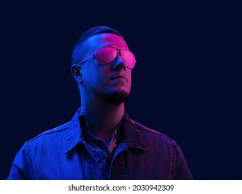Portrait young millennial man wearing denim jacket   sunglasses in neon pink studio light 