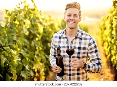 Portrait of a young, millennial vintner holding a glass and a bottle of organic bio red wine outdoors in a vineyard - Vine-growing, and wine-tasting concept in a rural winery - Powered by Shutterstock