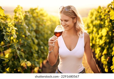 Portrait of a young, millennial woman holding and smelling a glass of organic bio red wine outdoors in a vineyard - Vine-growing, and wine-tasting concept - Powered by Shutterstock