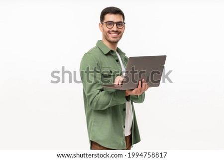 Portrait of young modern businessman standing holding laptop and looking at camera with happy smile, isolated on gray