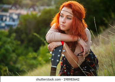 Portrait of young modern girl with bright red hair on the background of nature. Young woman with a guitar on a background sunset. Young woman hippie style. Bracket, quadrant. blurred background.
