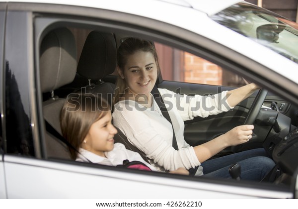 Portrait of young mother driving car to school\
with daughter