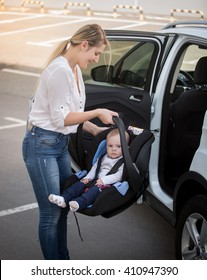 Portrait Of Young Mother Installing Car Child Seat With Baby