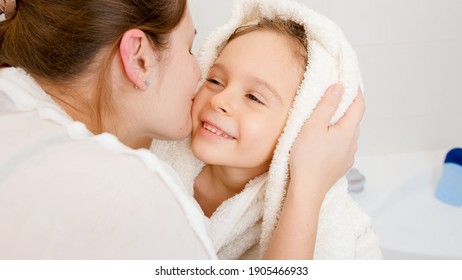 Portrait of young mother kissing her little son covered in white towel after washing in bath. - Powered by Shutterstock