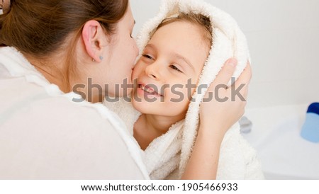 Portrait of young mother kissing her little son covered in white towel after washing in bath.