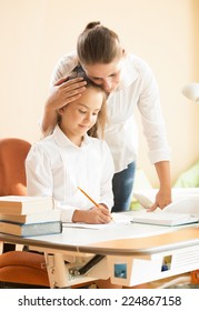 Portrait of young mother praising daughter doing homework at desk