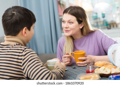 Portrait of young mother and son with tea talking at table indoors
