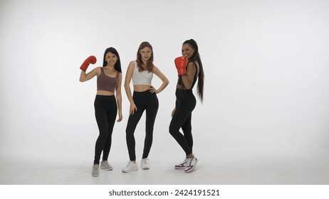 Portrait of young multiethnic models isolated on white studio background. Group of three positive multiracial girls posing in boxing gloves at camera. Multiethnic beauty concept. - Powered by Shutterstock