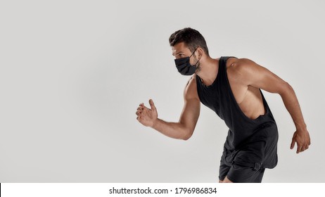 Portrait Of Young Muscular Caucasian Man Wearing Black Medical Mask Looking Aside While Ready To Run, Standing Isolated Over Grey Background. Health, Sports, Quarantine Concept. Web Banner