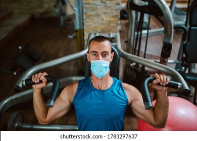 Portrait Of A Young Muscular Man With A Medical Face Mask Lifting Weights In The Gym. COVID 19 Coronavirus Protection