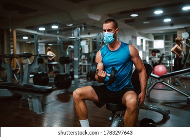 Portrait Of A Young Muscular Man With A Medical Face Mask Lifting Weights In The Gym. COVID 19 Coronavirus Protection