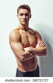 Portrait of a young muscular man with naked torso standing with arms crossed against white wall