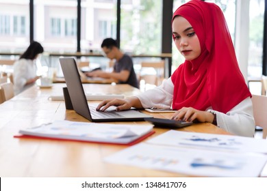 Portrait Of Young Muslim Business People Wearing Red Hijab Working With Calculator And Laptop In Cafe Or Coffee Shop.