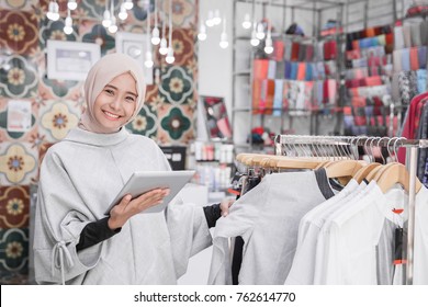 Portrait of a young muslim businesswoman with beautiful smile holding digital tablet while standing in her fashion boutique, female owner - Powered by Shutterstock