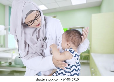 Portrait Of A Young Muslim Doctor Wearing Headscarf And Examining A Baby In The Hospital Room