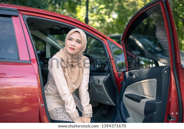 portrait of young muslim\
woman in hijab sitting on car seat with opened door. Female driver\
concept.