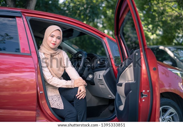 portrait of young muslim\
woman in hijab sitting on car seat with opened door. Female driver\
concept.