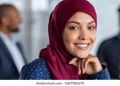 Portrait Of Young Muslim Woman Wearing Hijab In Office While Looking At Camera. Close Up Face Of Arabic Business Woman Covered With Headscarf Smiling. Successful Arab Businesswoman In Modern Office.