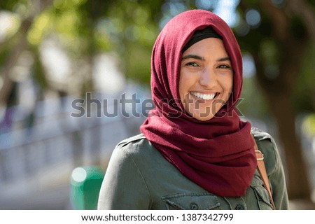 Portrait of young muslim woman wearing hijab head scarf in city while looking at camera. Closeup face of cheerful woman covered with headscarf smiling outdoor. Casual islamic girl at park.