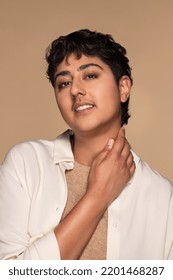 Portrait Of Young Non-binary Punjabi Person Smiling With Their Hand On Their Neck Posing Confidently On Neutral Background