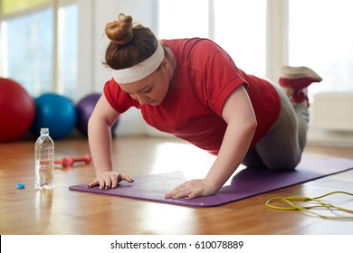 Portrait Of Young Obese Woman Working Out On Yoga Mat In Sunlit Fitness Studio: Performing Knee Push Up Exercise With Effort To Lose Weight